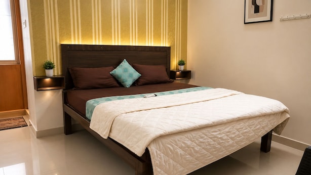 Una cama bien tendida con cubrecama acolchado, dos mesitas de noche con lámparas y una pared con rayas verticales.