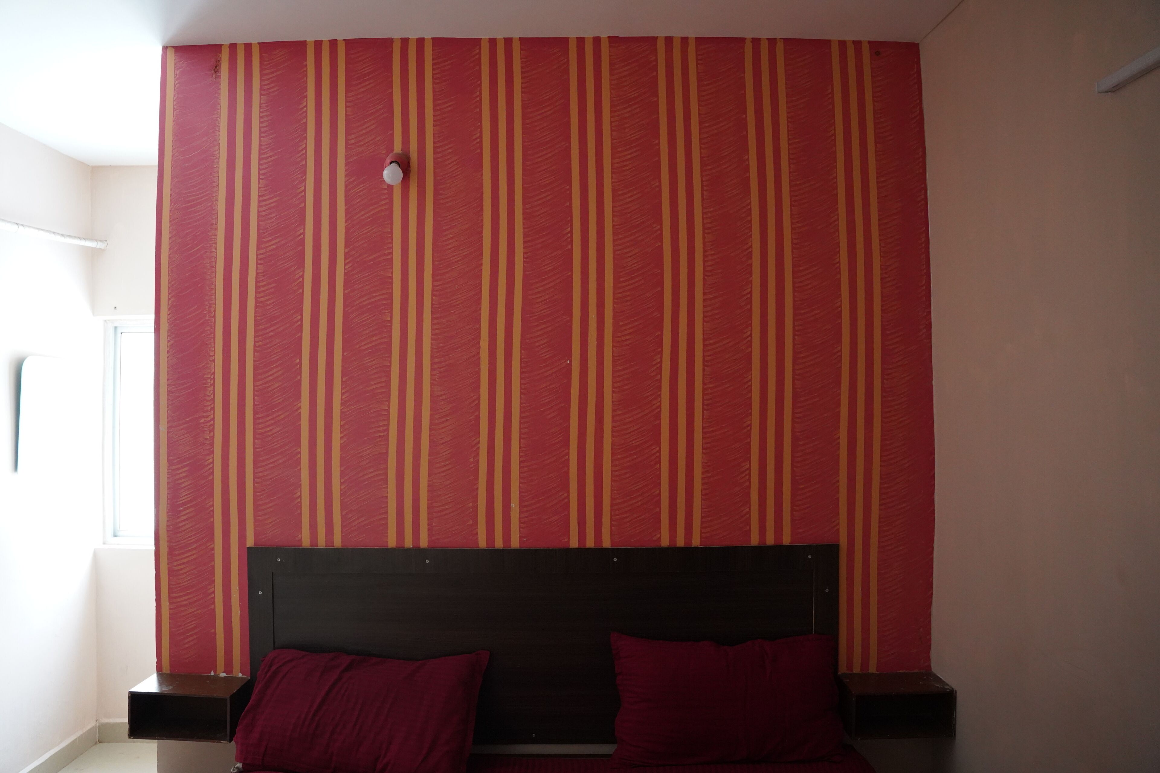 Una habitación con una pared a rayas, una cama con dos almohadas y una ventana.