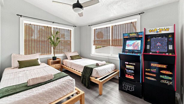Une chambre avec deux lits, un ventilateur de plafond et une borne d’arcade Pac-Man.