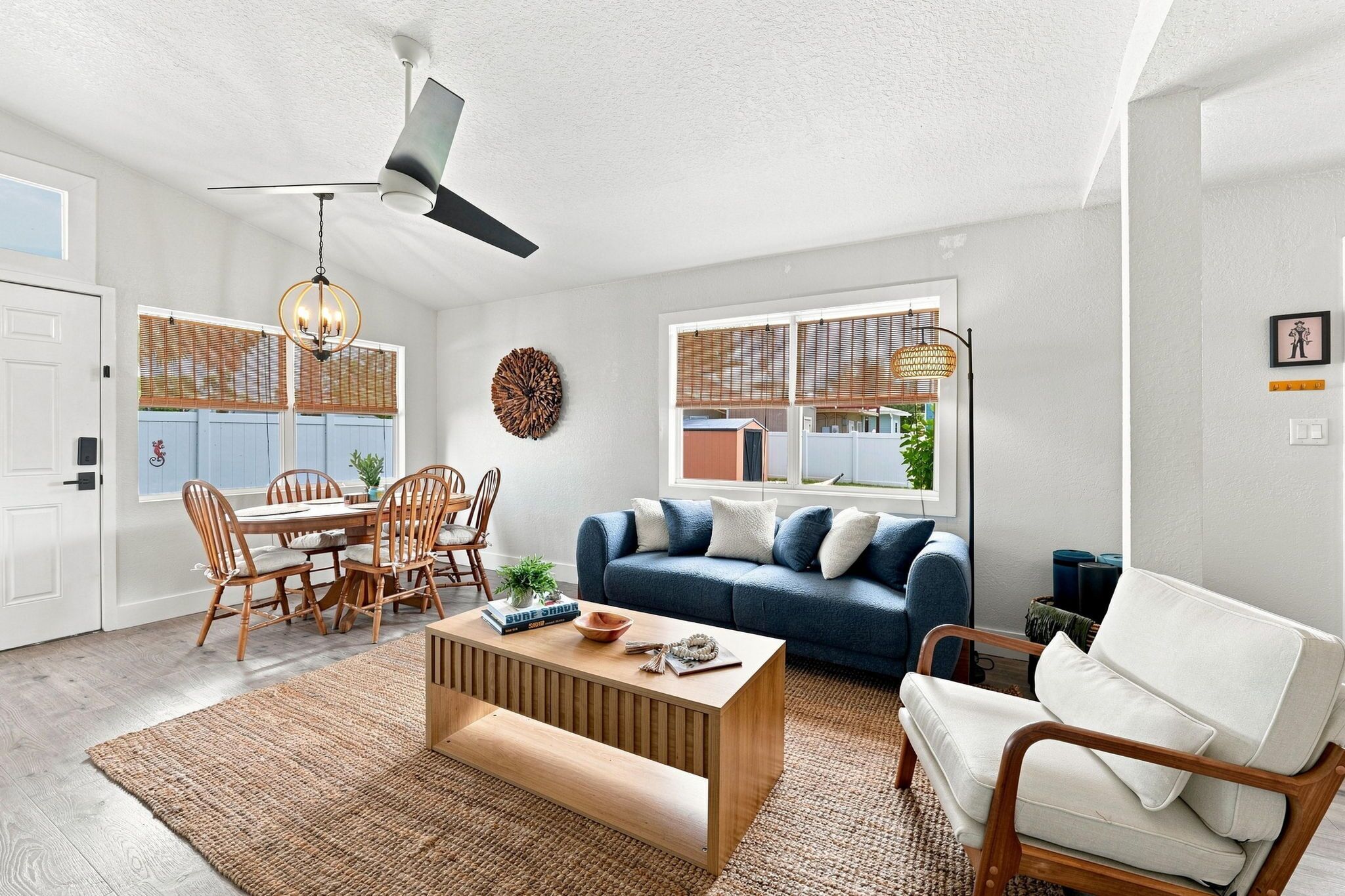 Una sala de estar moderna con comedor, ventilador de techo y amplios ventanales con persianas.