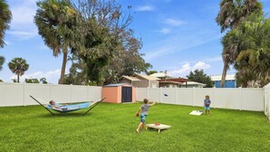 Un jardin avec un hamac, un petit abri de jardin et une maison en arrière-plan.