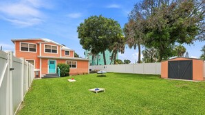 Un jardin à l’arrière d’une maison, avec une pelouse bien entretenue, une terrasse en bois et une maison dont la porte est peinte en turquoise.