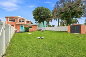 Un patio trasero residencial con un césped cuidado, una terraza de madera y una casa con puerta turquesa.