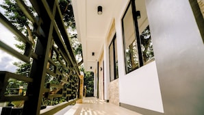 Un pasillo con vistas a árboles a través de una estructura celosíaca, que conduce a una habitación con un ventanal grande.