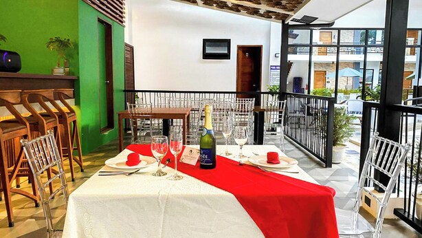 Un comedor con una mesa dispuesta para dos, una botella de champán y un camino de mesa rojo.