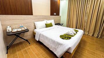Habitación de hotel con una cama, una mesita de noche con hervidor y botellas de agua, un cabecero y una cortina.