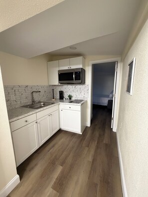 A compact kitchen with white cabinets, a microwave, a sink, and a coffee maker. - Loft Living: 4 to 5 minutes from Bush Gardens (Tampa)