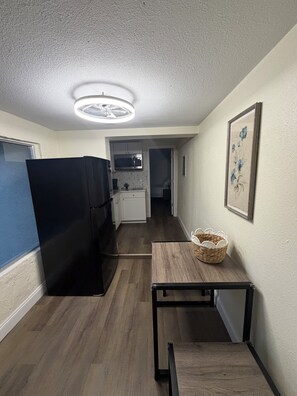 A compact kitchen with a refrigerator, microwave, and a small dining table with a basket. - Loft Living: 4 to 5 minutes from Bush Gardens (Tampa)