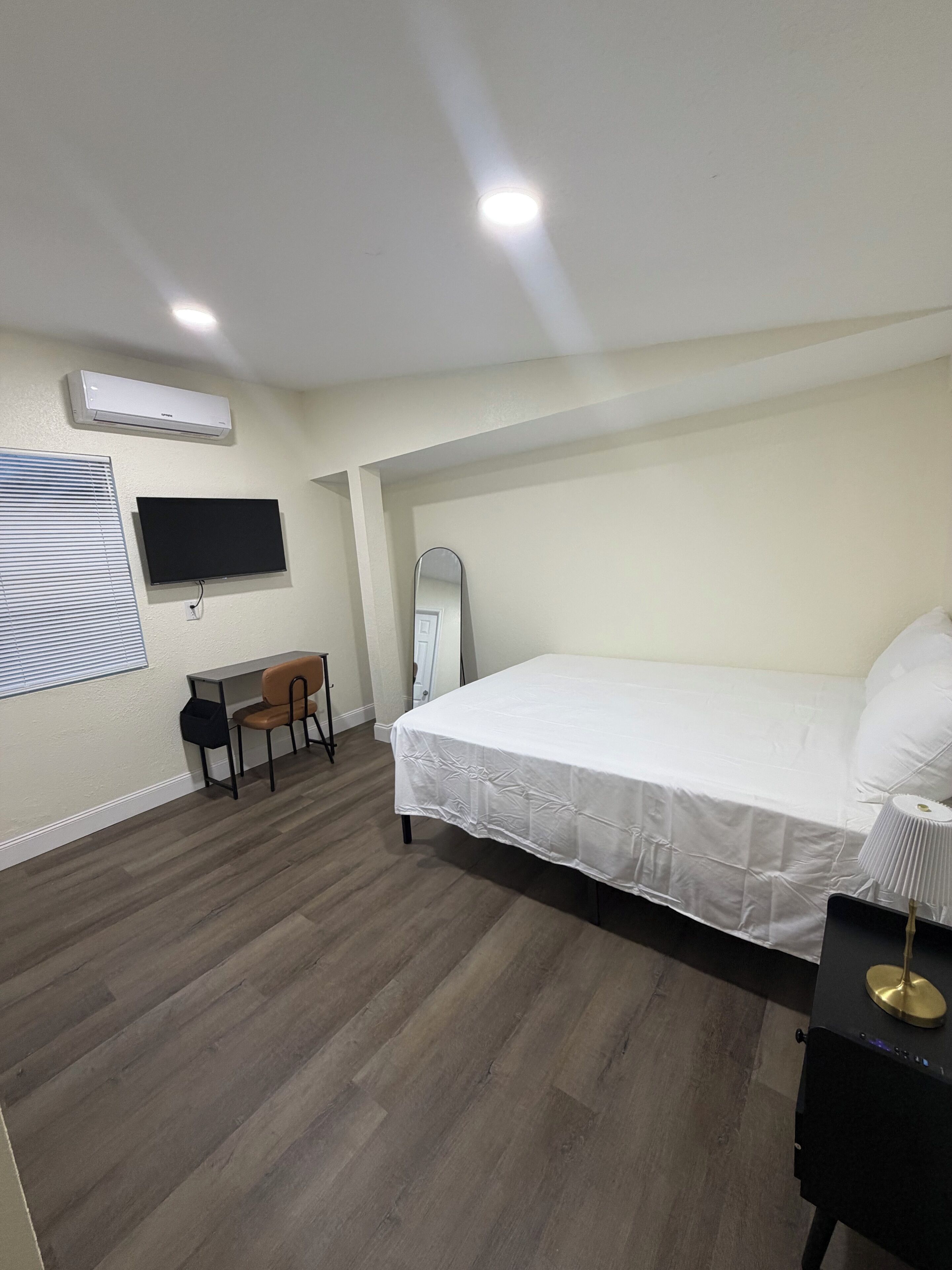 Un dormitorio con cama, escritorio, silla, espejo y televisor.