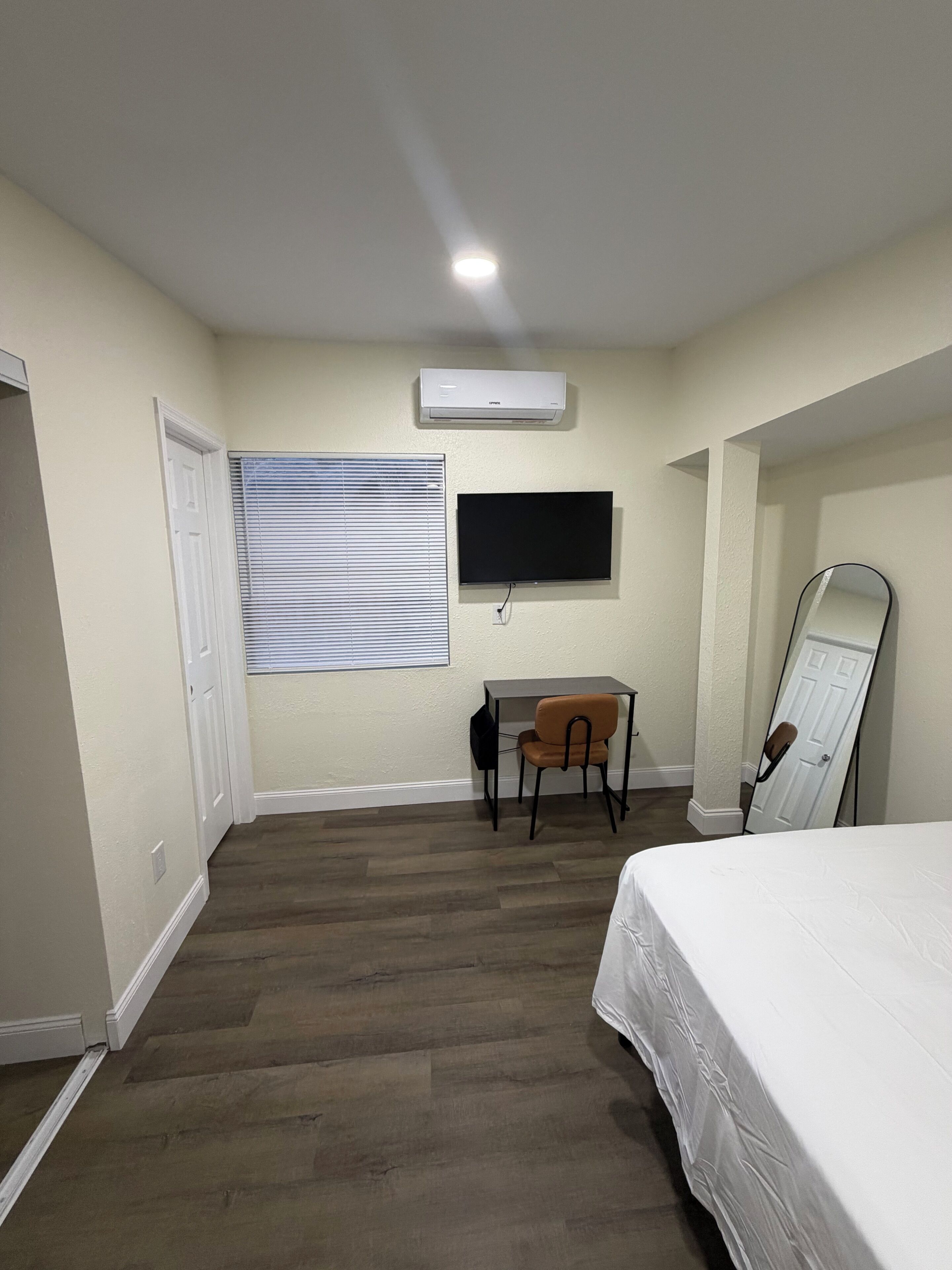 Une chambre à coucher comprenant un lit, un bureau, une chaise, un téléviseur à écran plat et un appareil de climatisation.