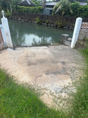 A concrete pathway leading to a water body, surrounded by greenery and a stone wall. - Villa Noa Vai • Swimming Pool & Lagoon Access by Kayak (papetoai)