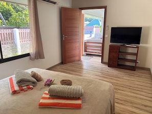 Quarto de hotel com uma cama, televisão, porta de madeira e vista para o exterior.
