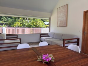 Um espaço de estar moderno ao ar livre, com mesa de madeira, cadeiras brancas e sofá bege.