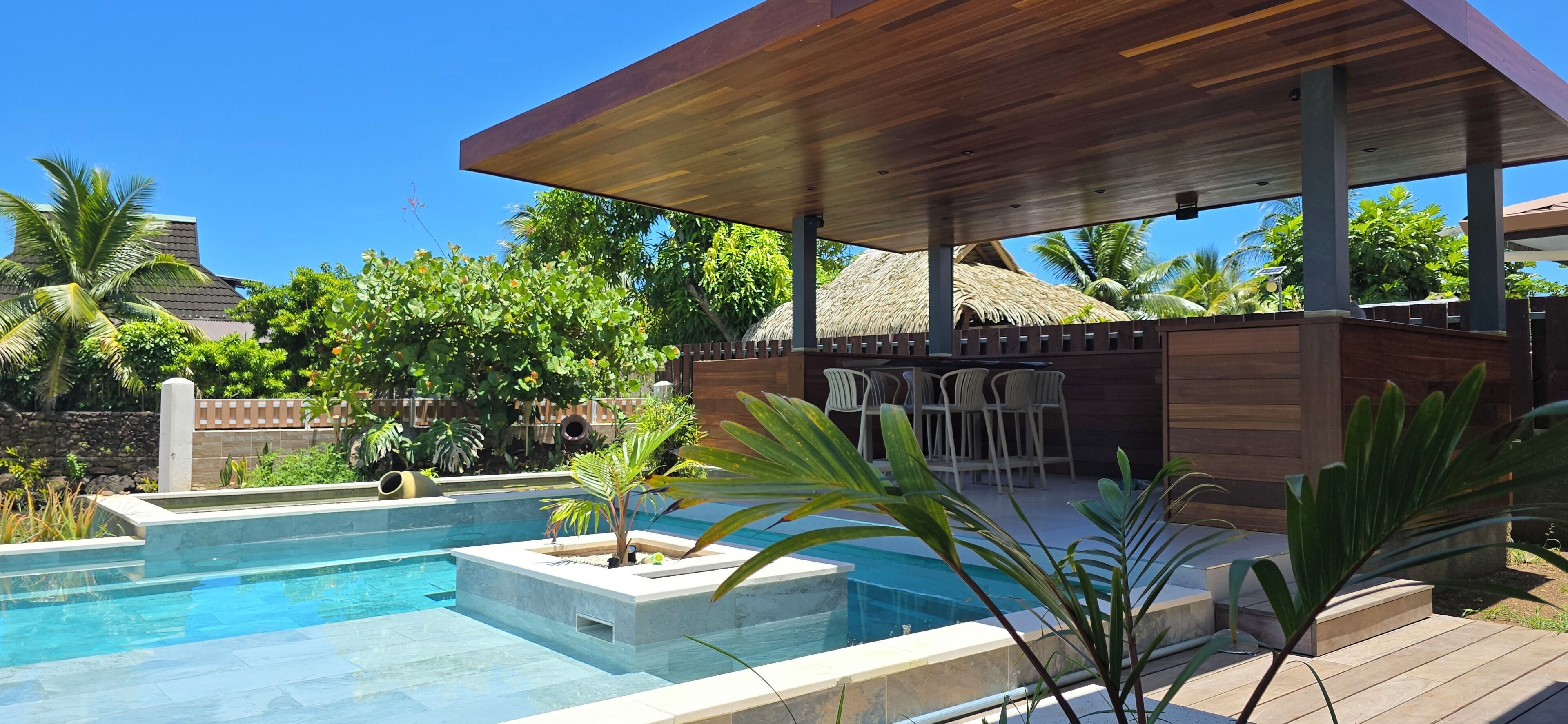 A pool area with a wooden deck, lounge chairs, and a thatched-roof structure.