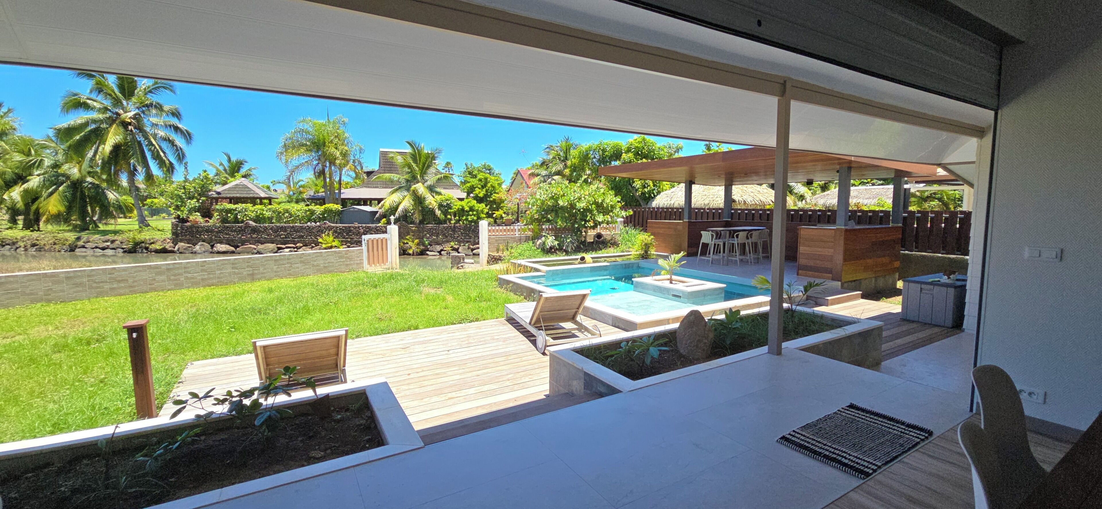 Un área de piscina exterior moderna con cubierta de madera, sillones de descanso y un espacio de estar techado.