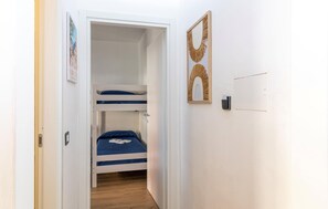 Ein schmaler Flur, der zu einem Raum mit einem Etagenbett, einem gerahmten Spiegel und einem Lichtschalter an der Wand führt.