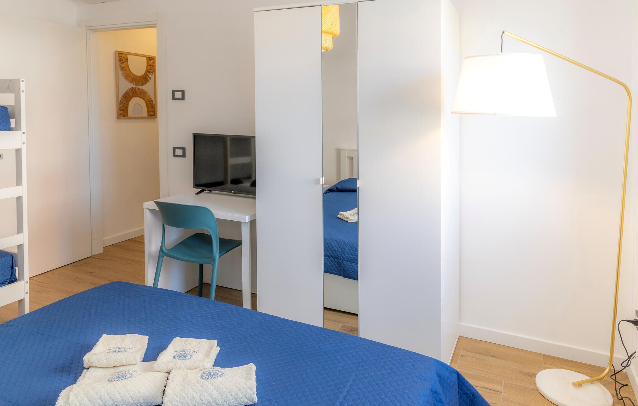 Una camera da letto con un letto, una scrivania, una sedia, una TV e una lampada da terra.