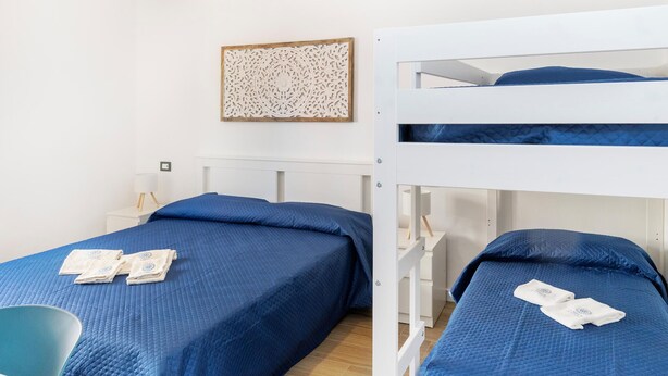 Ein Zimmer mit zwei Etagenbetten, beide mit blauer gesteppter Bettdecke und Kissen. Darüber befindet sich eine dekorative Wandverkleidung.