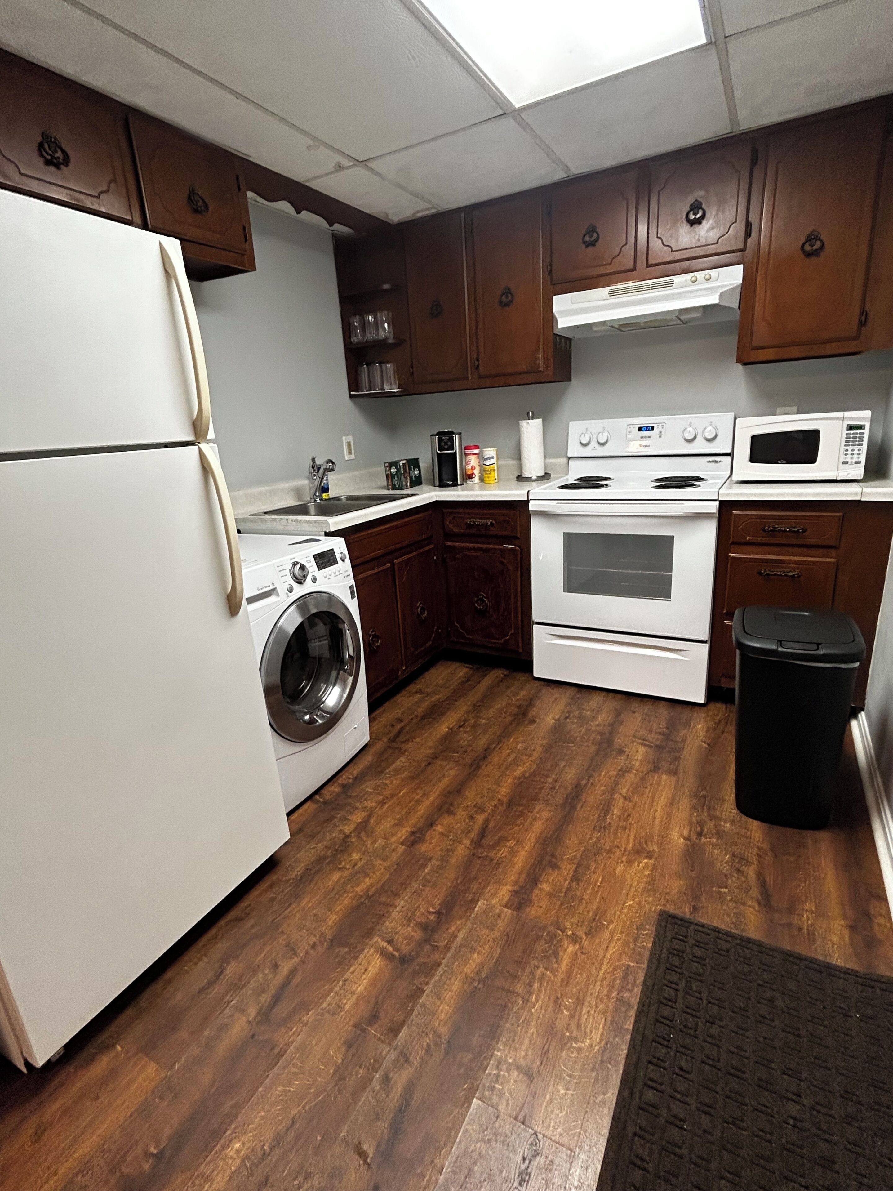 Una cocina con armarios de madera, un refrigerador, una lavadora, una estufa y un microondas.