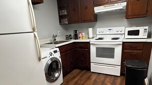 Una cocina con armarios de madera, un refrigerador, una lavadora, una estufa y un microondas.