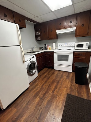 A kitchen with wooden cabinets, a refrigerator, a washing machine, a stove, and a microwave.