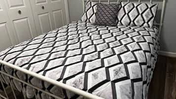 A bed with a geometric patterned bedspread and matching pillows, a metal headboard, and a white door in the background.