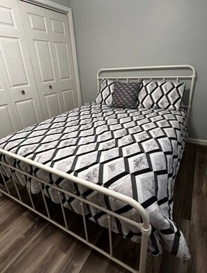 A bed with a geometric patterned bedspread and matching pillows, a metal headboard, and a white door in the background.