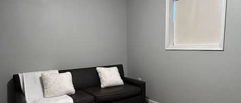 A room with a dark-colored sofa, a white throw blanket, and a wooden coffee table with a white base.