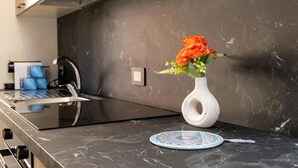 A kitchen counter with a white vase containing orange flowers, a decorative plate, and a coffee machine. - Maison marina Suite - Mykonos (Paola)