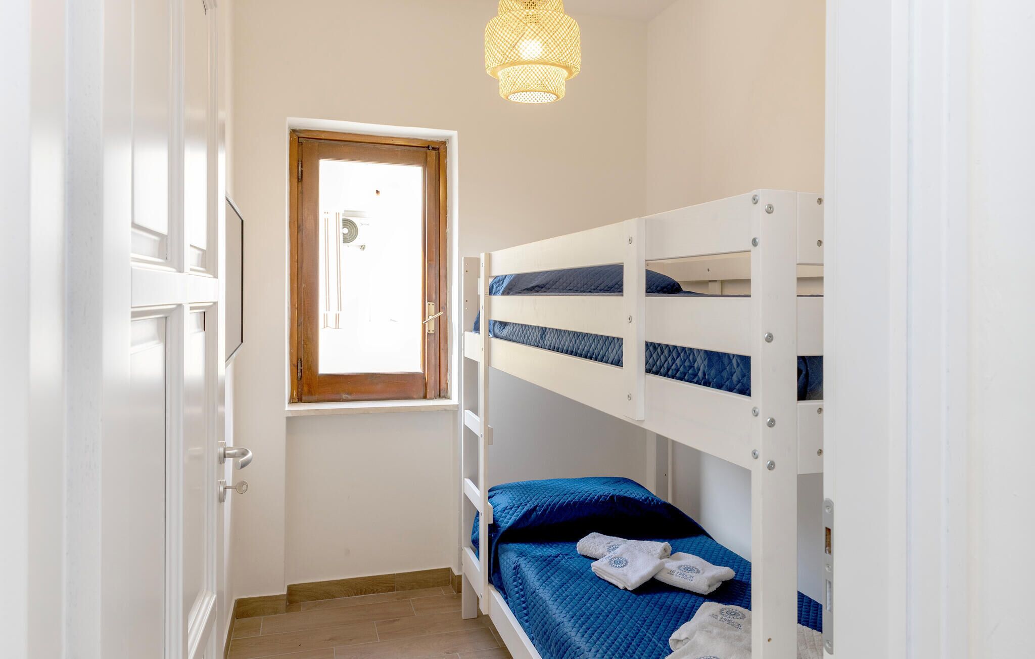 A bunk bed room with a door, a window, and a hanging light fixture.