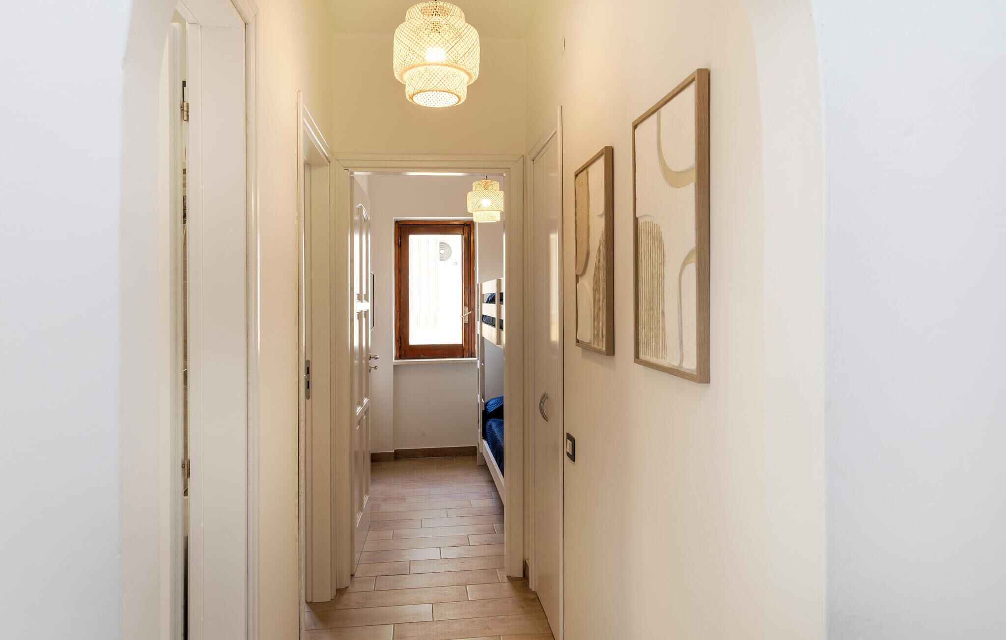 Un corridoio stretto con pavimento in legno, una porta in fondo e un lampadario.