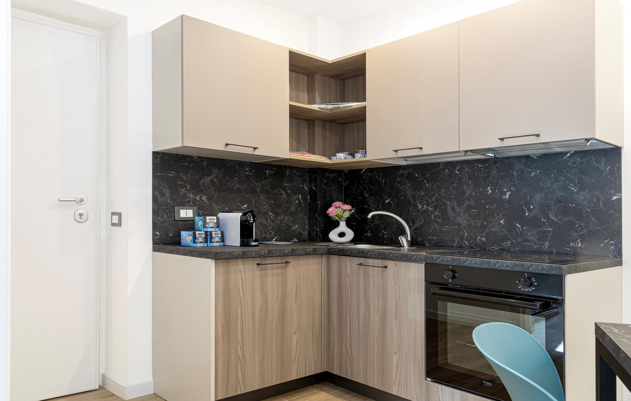 Una cucina compatta con un piano di lavoro in marmo nero, forno integrato e un armadietto in legno.