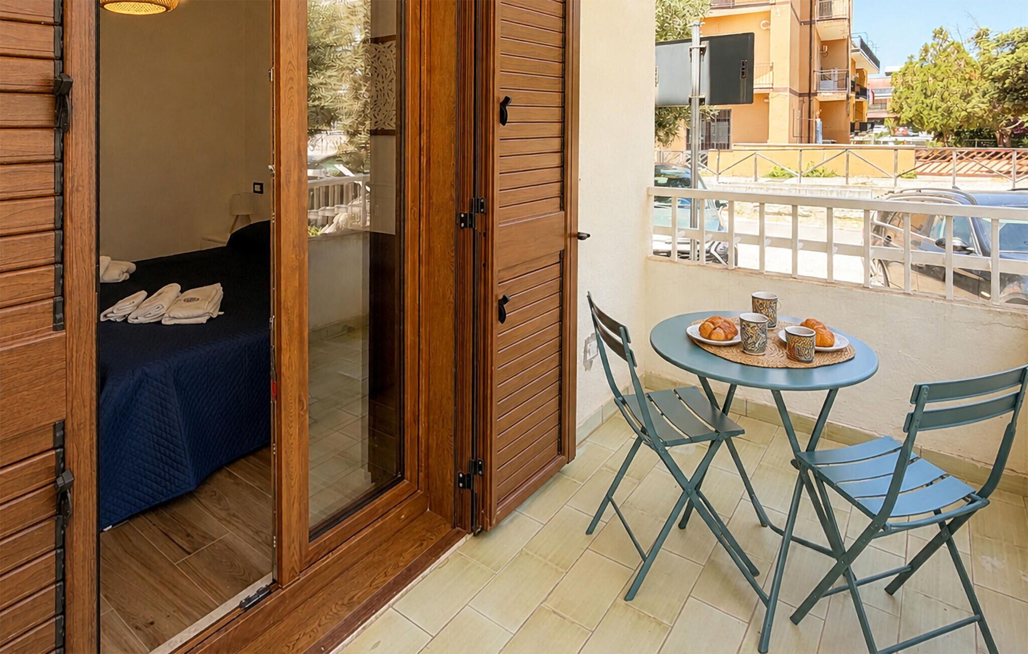 Un balcone con un letto, un tavolo e una sedia, e vista sulla strada.