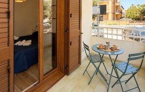 Un balcon avec un lit, une table et une chaise, et une vue sur la rue.