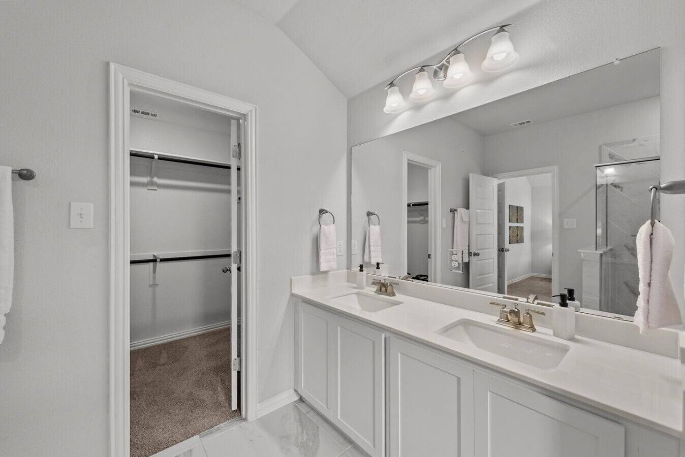 A modern bathroom with a walk-in closet, a large mirror, and a double sink vanity.