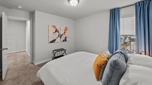 Ein Hotelzimmer mit einem Bett, einem Nachttisch, einem Fenster mit Vorhängen und einem Bild an der Wand.
