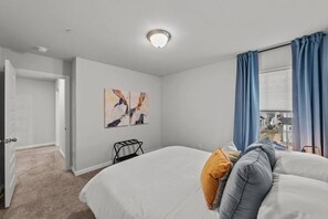 Ein Hotelzimmer mit einem Bett, einem Nachttisch, einem Fenster mit Vorhängen und einem Bild an der Wand.