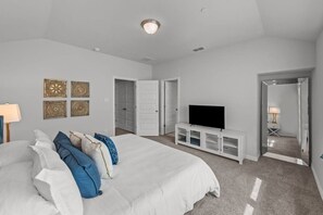 Ein Schlafzimmer mit einem großen Bett, einem Fernseher auf einem weißen Schrank und einer Tür zu einem anderen Raum.