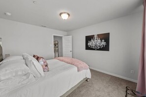 Un dormitorio con cama, una puerta, una araña y un cuadro colgado en la pared.