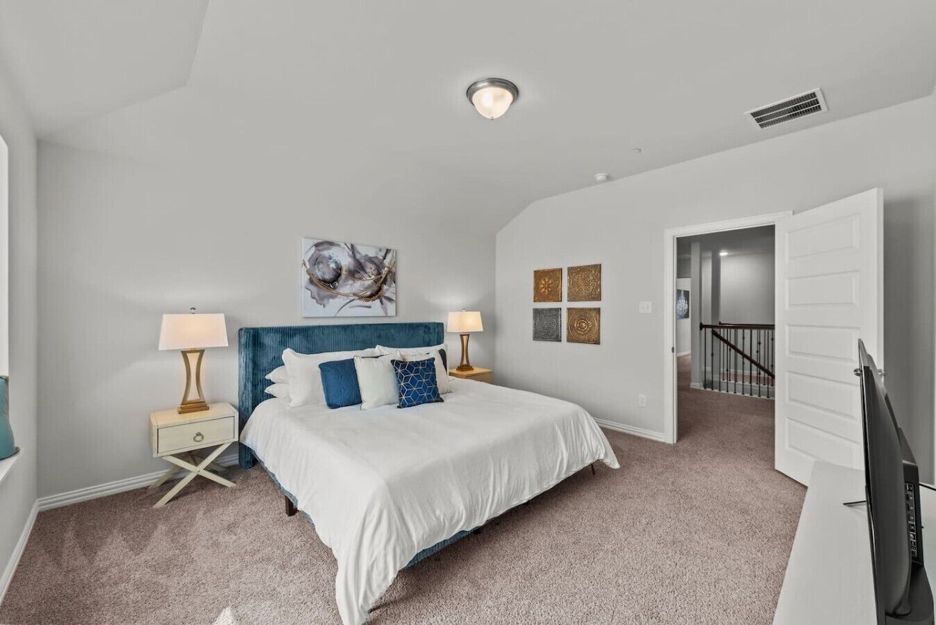 A bedroom with a bed, two bedside tables, a nightstand, a ceiling light, and a door leading to another room.