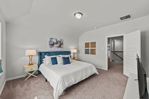 A bedroom with a bed, two bedside tables, a nightstand, a ceiling light, and a door leading to another room. - Lewisville Lake Urban Escape (Lewisville)