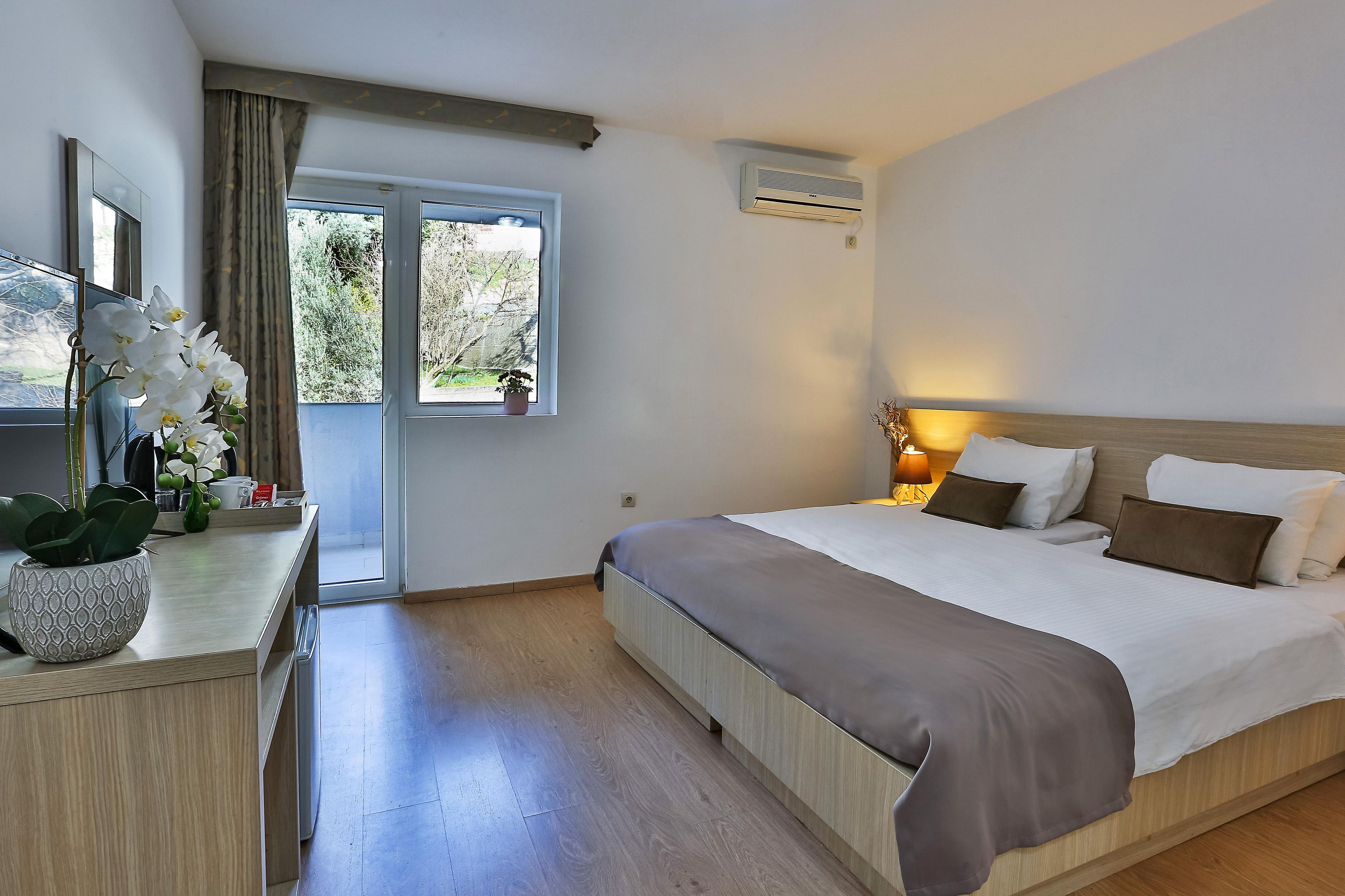 Una habitación de hotel con cama, mesita de noche, lámpara y ventana con cortinas.