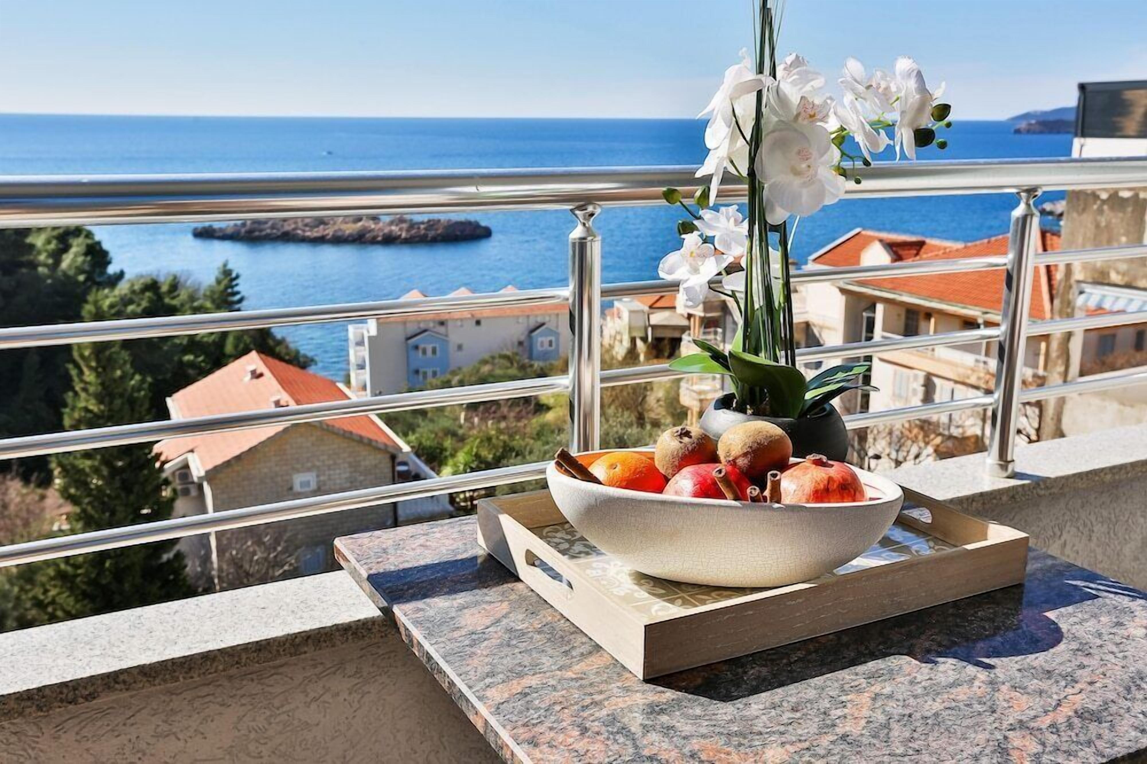 Un bol de fruta en un balcón con vistas al mar y edificios.