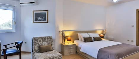 A bedroom with a bed, bedside tables, a chair, an air conditioner, a framed picture, and a window.