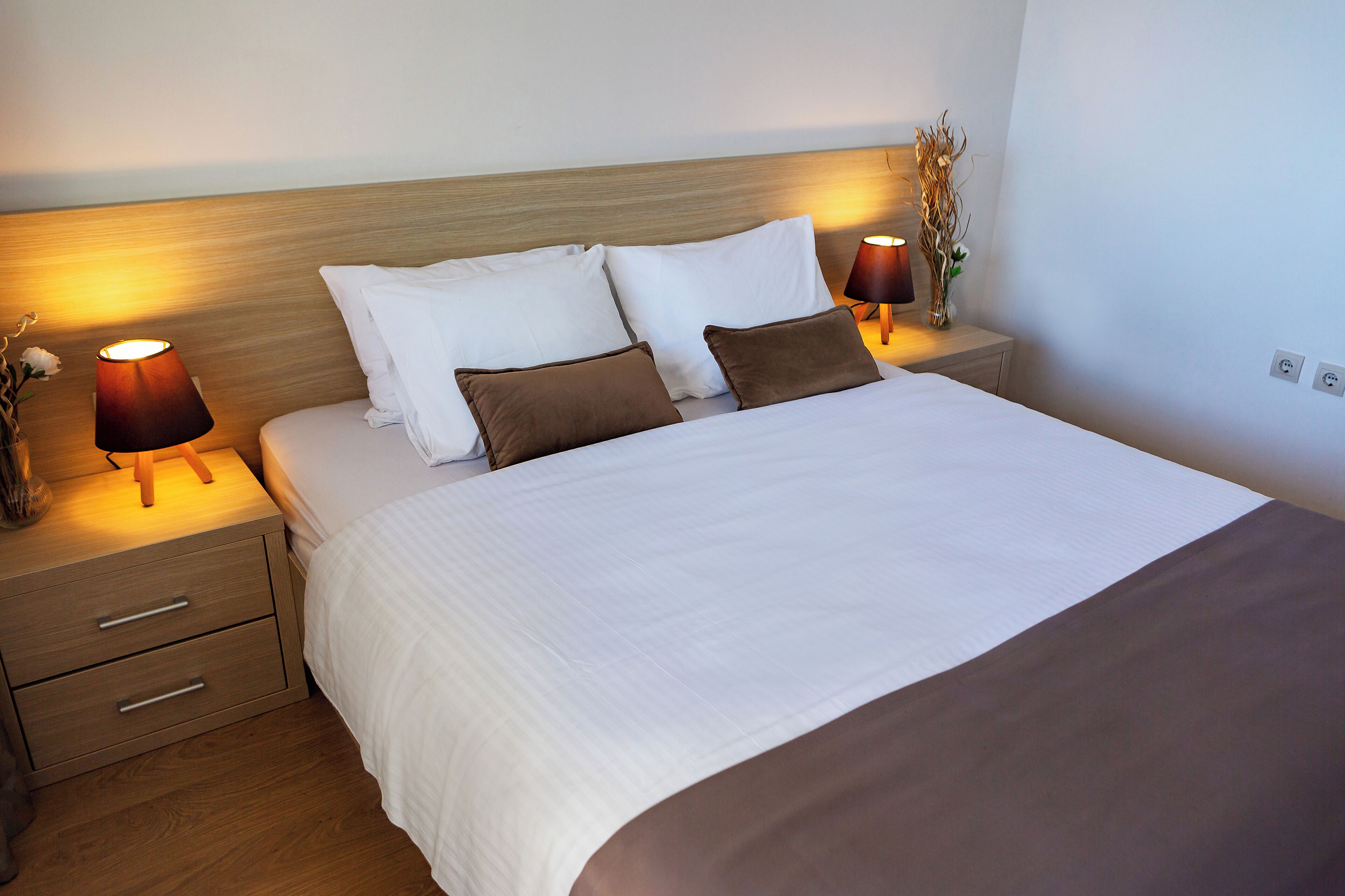 A neatly made bed with white and brown bedding, two bedside tables with lamps, and a wooden headboard.