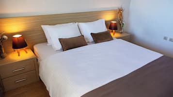 A neatly made bed with white and brown bedding, two bedside tables with lamps, and a wooden headboard.