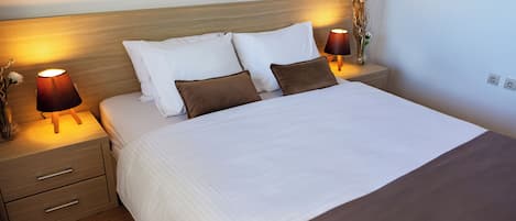 Una cama bien hecha con ropa de cama blanca y marrón, dos mesitas de noche con lámparas y un cabecero de madera.
