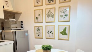 Eine moderne Küche mit Esstisch, Stühlen, einem Kühlschrank, einer Mikrowelle und gerahmten Pflanzenbildern an der Wand.