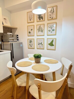 A modern kitchen with a dining table, chairs, a refrigerator, a microwave, and framed botanical prints on the wall. - Modern 1BR Staycation in Acqua Private Residences (Mandaluyong City)