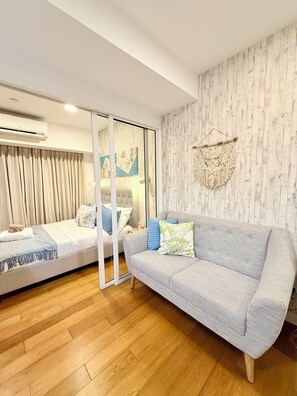 A modern bedroom with a bed, a sofa, a wooden floor, and a wall-mounted air conditioner. - Modern 1BR Staycation in Acqua Private Residences (Mandaluyong City)